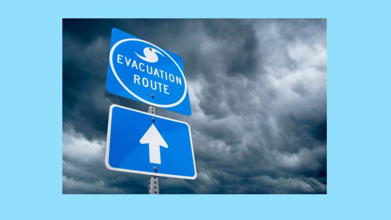 Blue emergency evacuation sign with backdrop of storm clouds