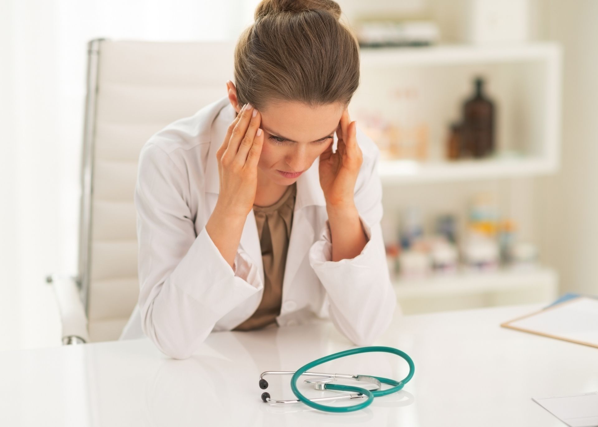 Veterinarian with elbows on table massaging her temples. Stethoscope on table in front of her