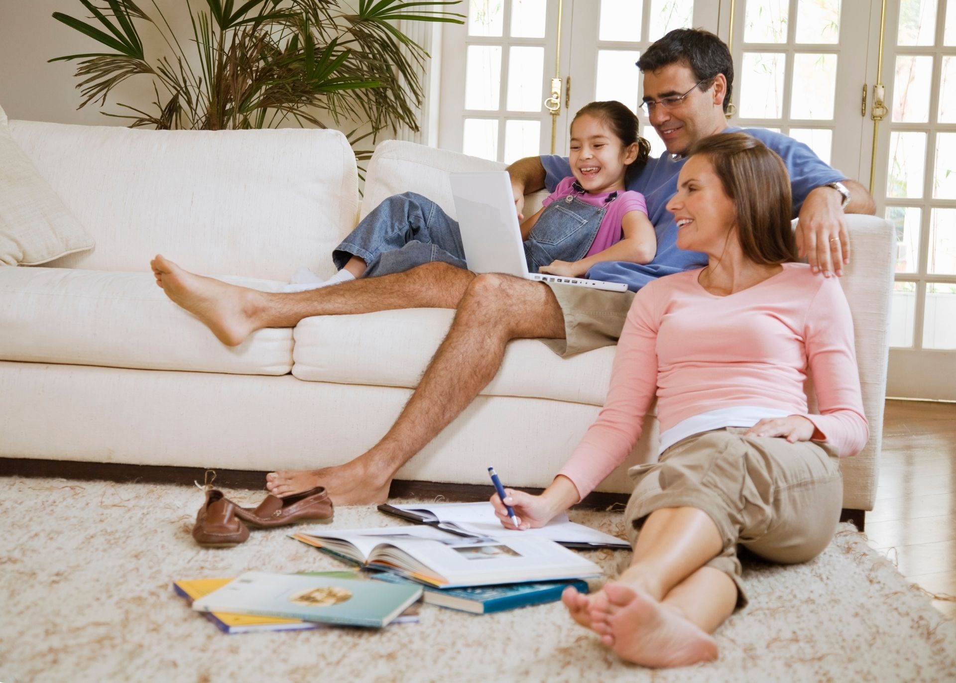 Smiling family on sofa and floor surrounded by books and computers. They're studying something.